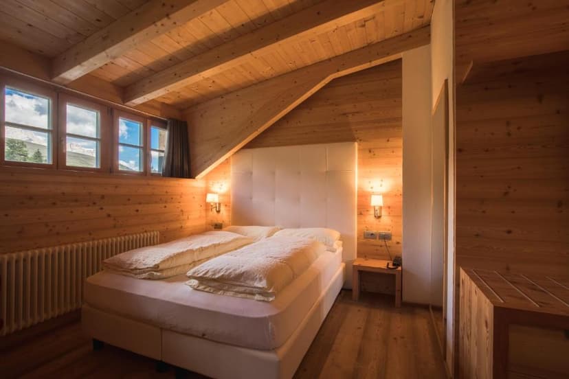 Hotel bedroom with wood paneling, white bed, and mountain view through windows