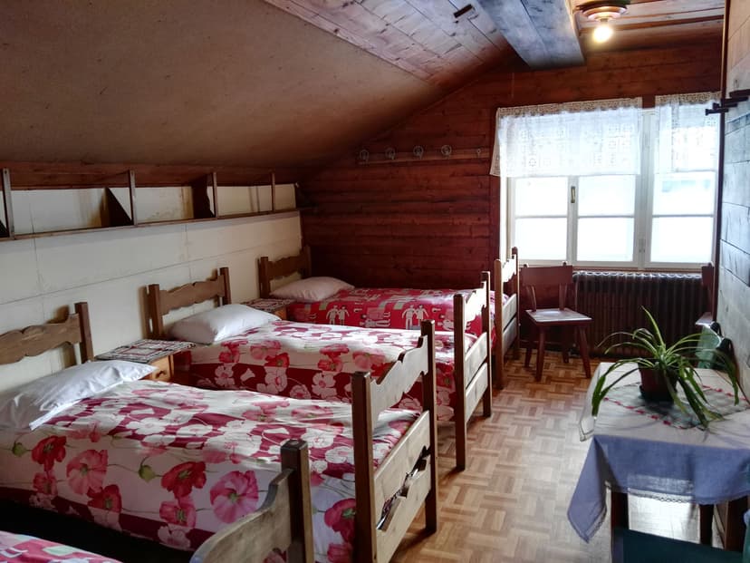 Dormitory room with wooden beds, floral bedding, and sloped wood-paneled ceiling at Rifugio Castiglioni Marmolada.