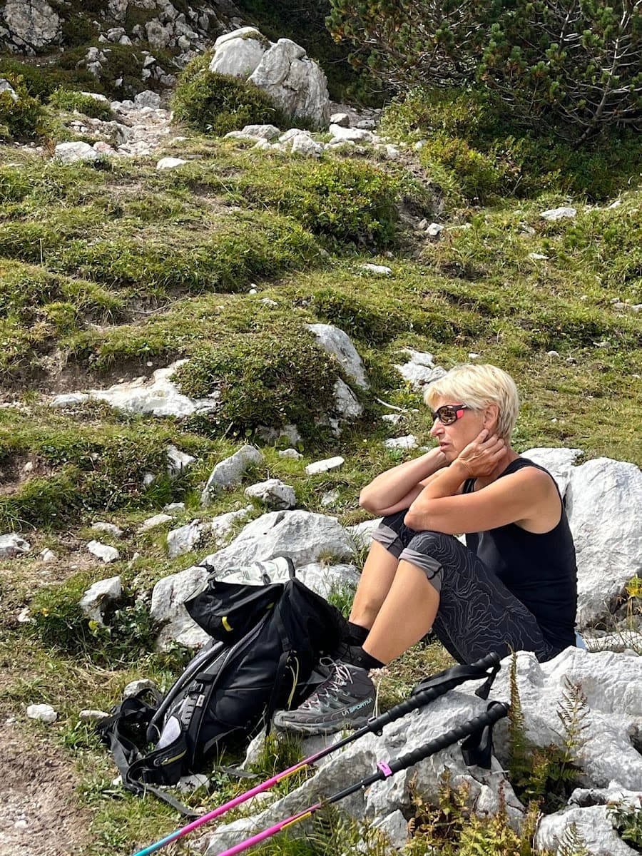 Hiker resting on rocky alpine slope with backpack and trekking poles nearby