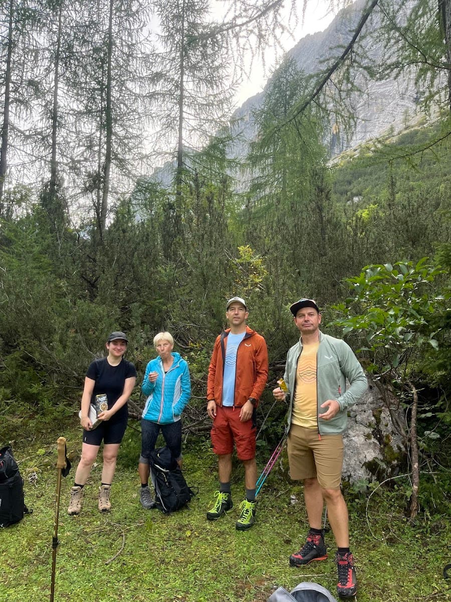 Hikers taking a break in a lush forest with tall trees and a rocky mountain backdrop