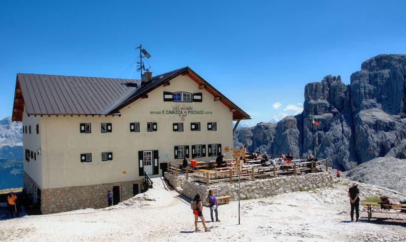 Rifugio F. Cavazza al Pisciadù mountain hut with outdoor dining near tall rocky peaks.