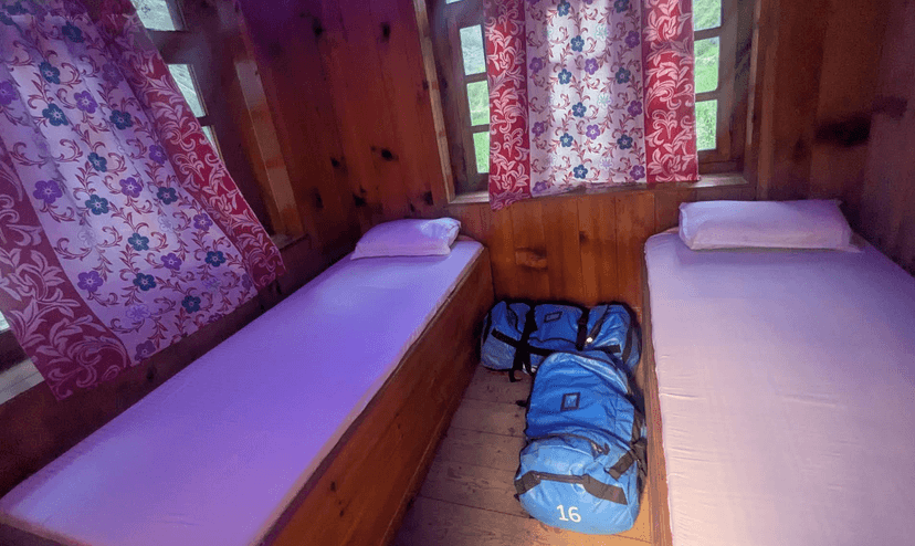 Twin beds in rustic wooden guest house room with floral curtains and blue duffel bags.