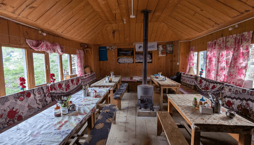 Wooden interior of a Himalayan lodge dining area with long tables, benches, and a central wood stove.