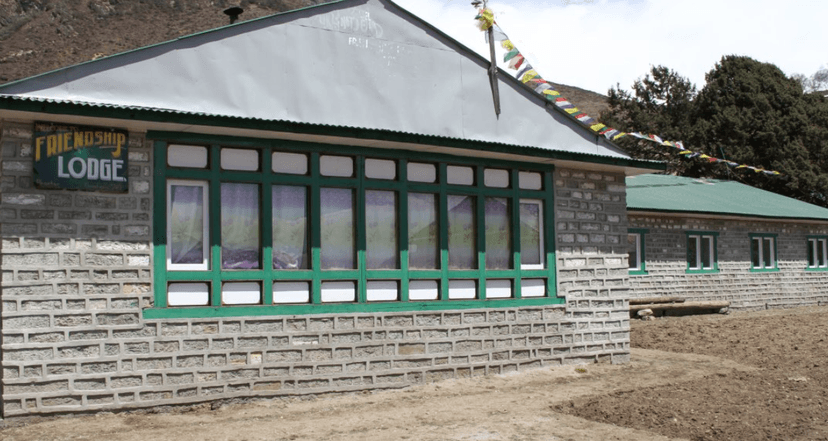 Friendship Lodge in Phortse with stone walls, green window frames, and prayer flags near mountains.