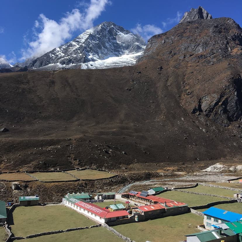 Machhermo Lodge and Bakery buildings in a green valley below massive rocky, snow-capped Himalayan mountains.