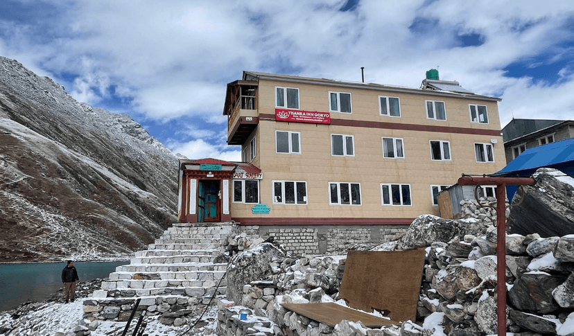 Thanka Inn Gokyo building near snowy mountain slope and turquoise lake in winter