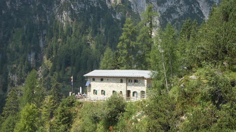 Rifugio Treviso stone mountain hut surrounded by dense green forest and steep cliffs