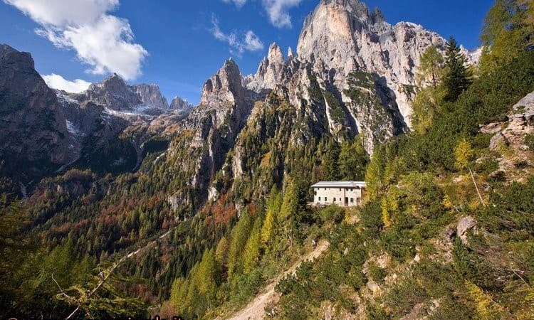 Rifugio Treviso mountain hut nestled on a steep slope below jagged Dolomite peaks in autumn.