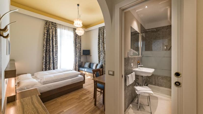 Hotel room with wooden floors, double bed, seating area, and visible bathroom sink and shower.