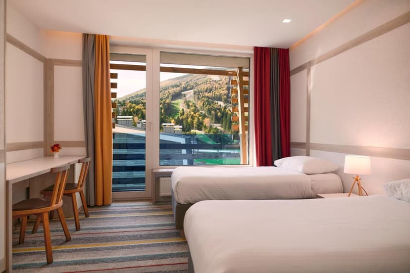 Twin hotel room with beds and desk overlooking forested mountain slope at Hotel Han Bjelašnica.
