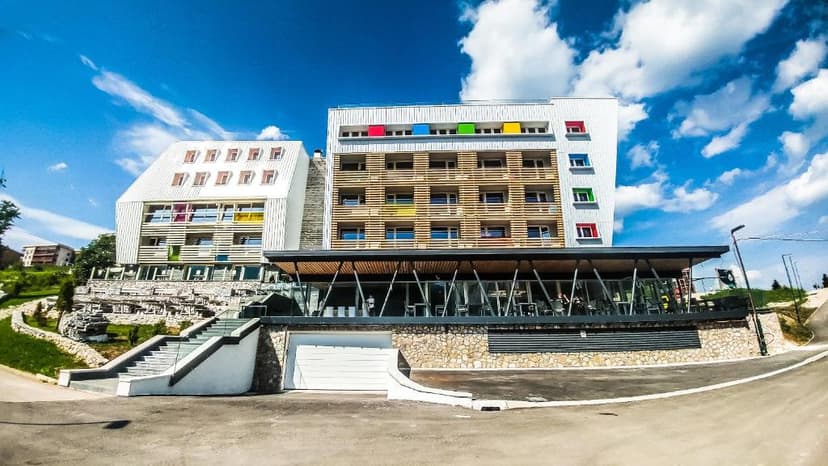 Modern hotel building with colorful window accents under a bright blue, cloudy sky at Hotel Han Bjelašnica.