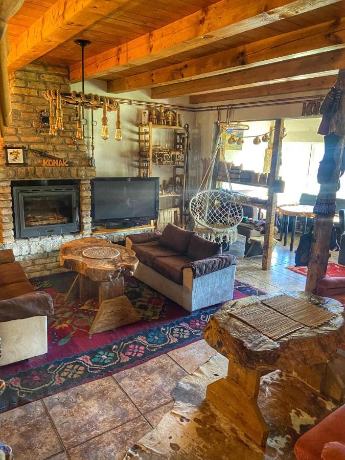Rustic living room in Konak Umoljani with stone fireplace, wood beams, and tree stump tables.