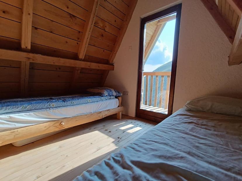 Attic bedroom with wood paneling, two beds, and balcony view of mountains