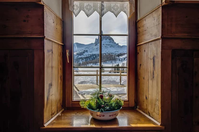 Window view of Rifugio Croda da Lago with snow-covered mountains and pine centerpiece.