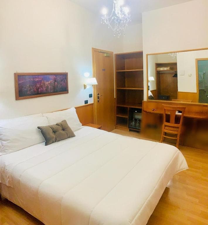 Hotel room with white bedding, wood furniture, mirror, and crystal chandelier lighting