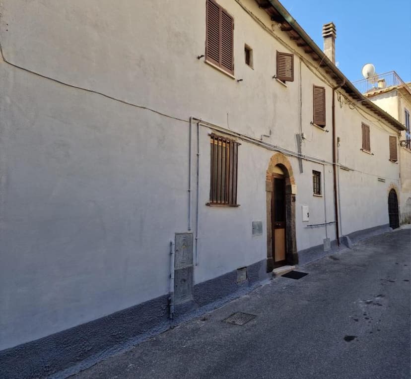 Light stucco building facade with brown shutters lining a narrow, paved street under clear sky.