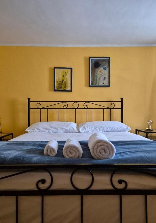 Bedroom with yellow walls, black metal bed frame, white linens, and rolled white towels.