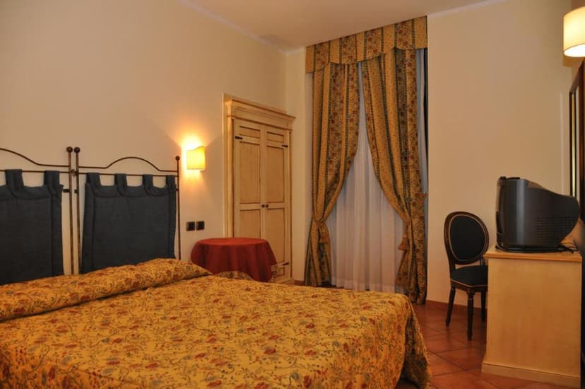 Hotel room with yellow floral bedspread, dark headboard, and patterned gold curtains.