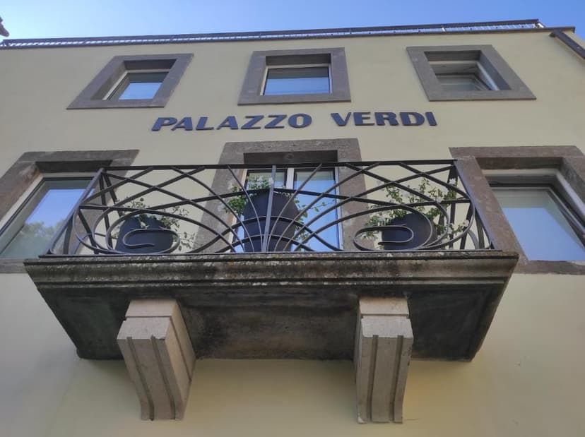 Palazzo Verdi building facade with balcony, wrought iron railing, and windows under blue sky in Viterbo.