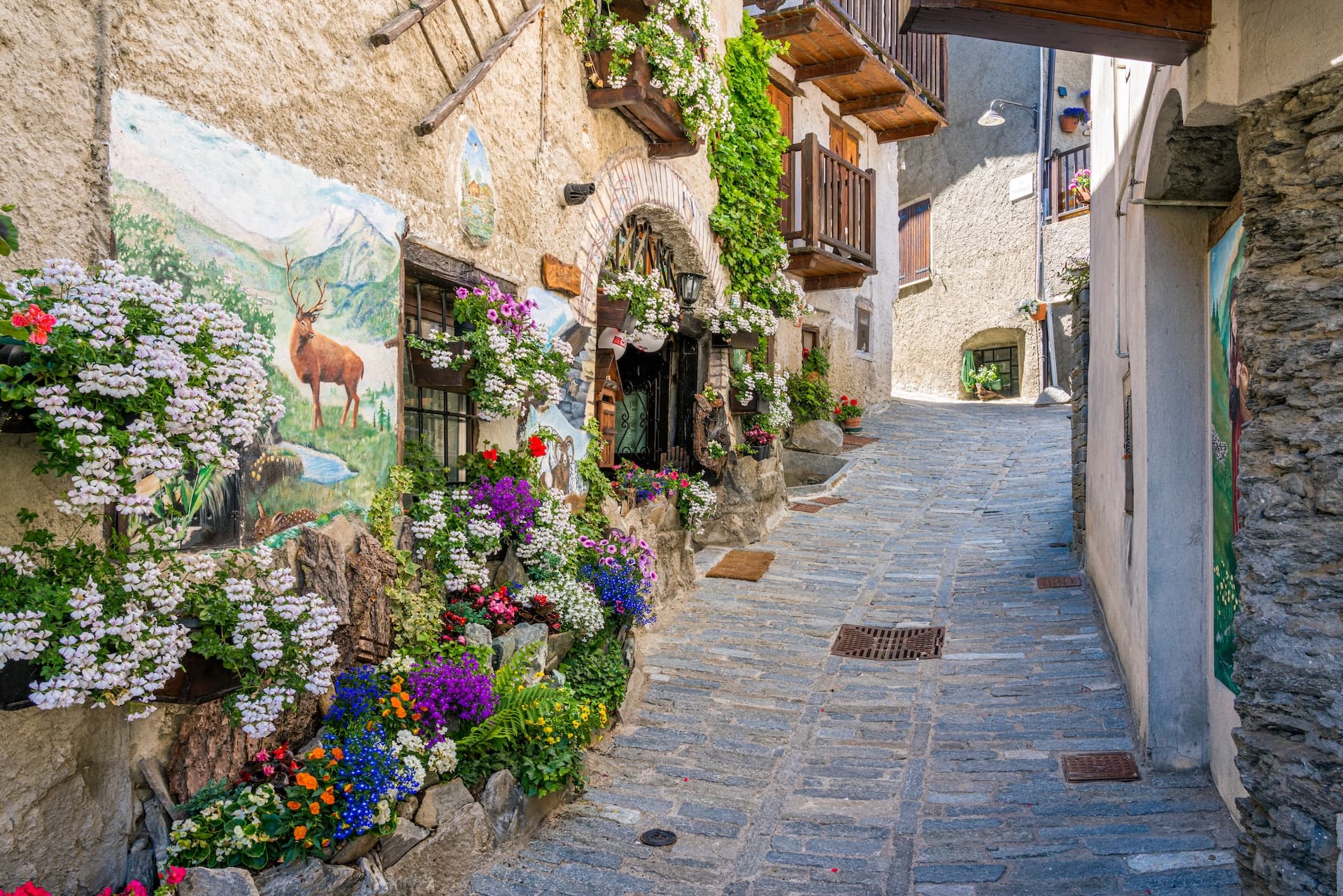 Cobblestone alley in a mountain village decorated with abundant colorful flowers and a deer mural.