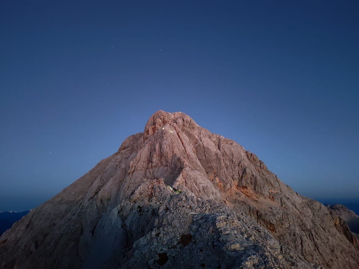Rocky mountain peak illuminated at dusk against a deep blue sky with visible stars
