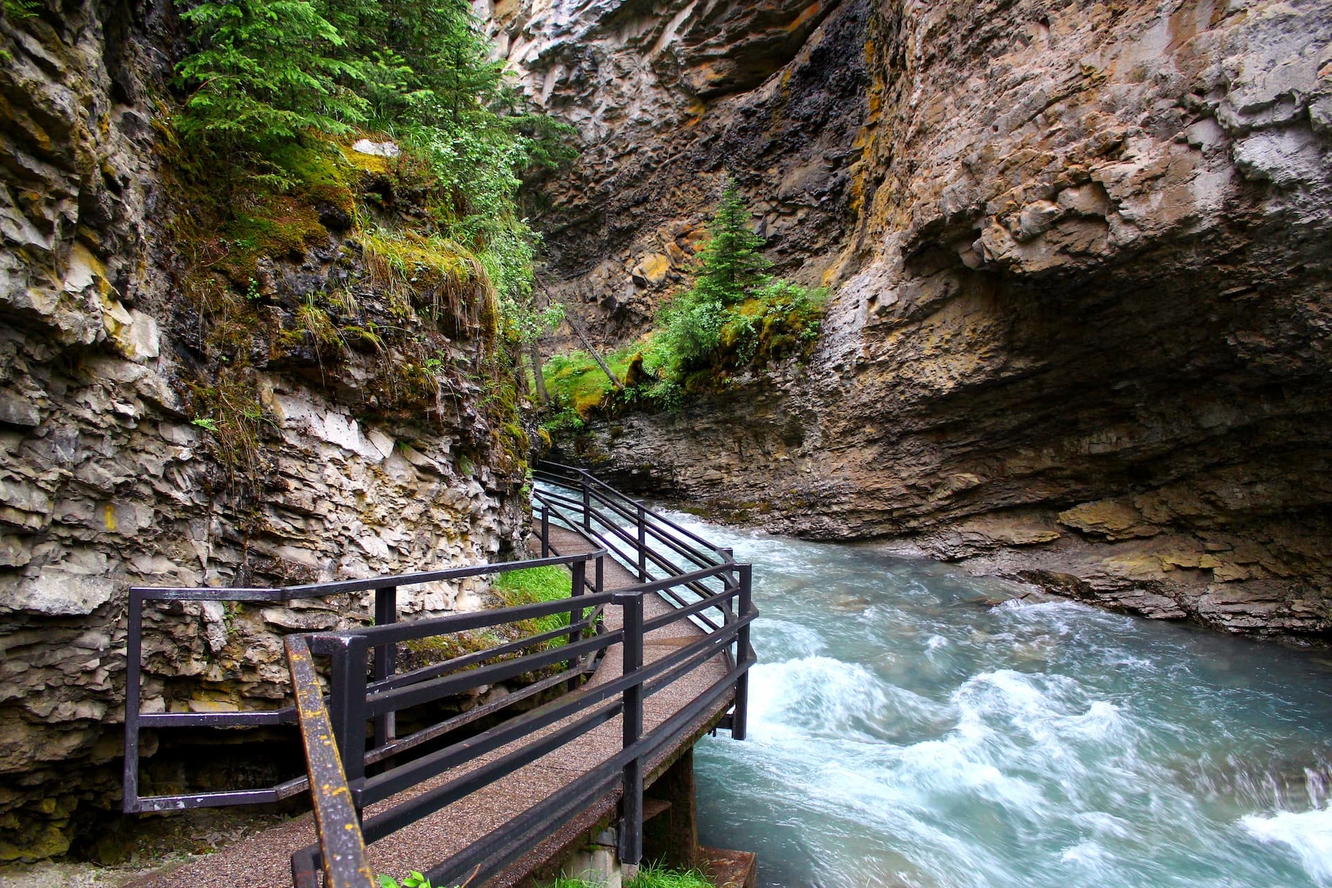 Hiking path along rushing river in a narrow canyon with steep rocky walls