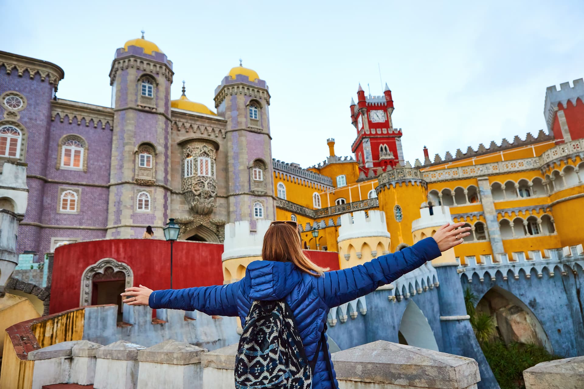 Tourist with arms outstretched facing colorful Pena Palace in Sintra, Portugal