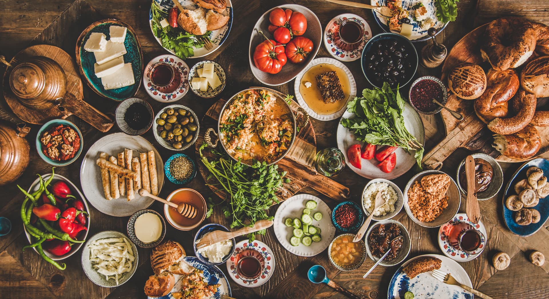 Abundant Turkish breakfast spread with eggs, cheese, olives, honey, tomatoes, and bread on a wooden table.
