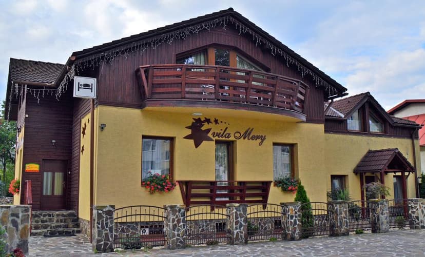Vila Mery guesthouse in Poprad with yellow facade, dark wood trim, and stone fence.