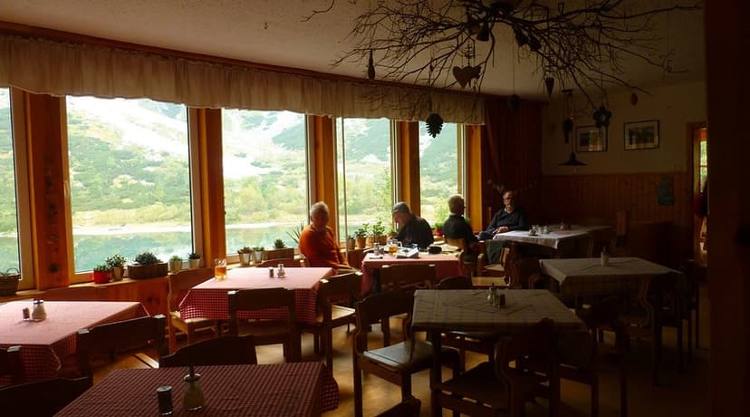 Diners inside Zelene Pleso Hut with view of mountain lake and slopes.