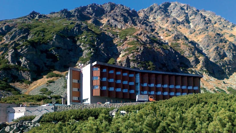 Hotel Sliezsky Dom nestled against rugged, scrub-covered mountains under a clear blue sky.