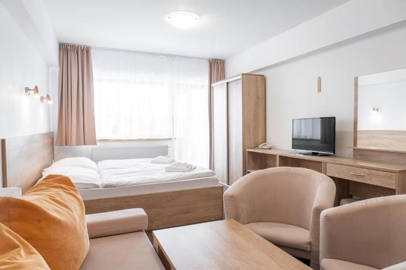 Bright hotel room with wooden furniture, white bedding, and light pink seating near a large window.