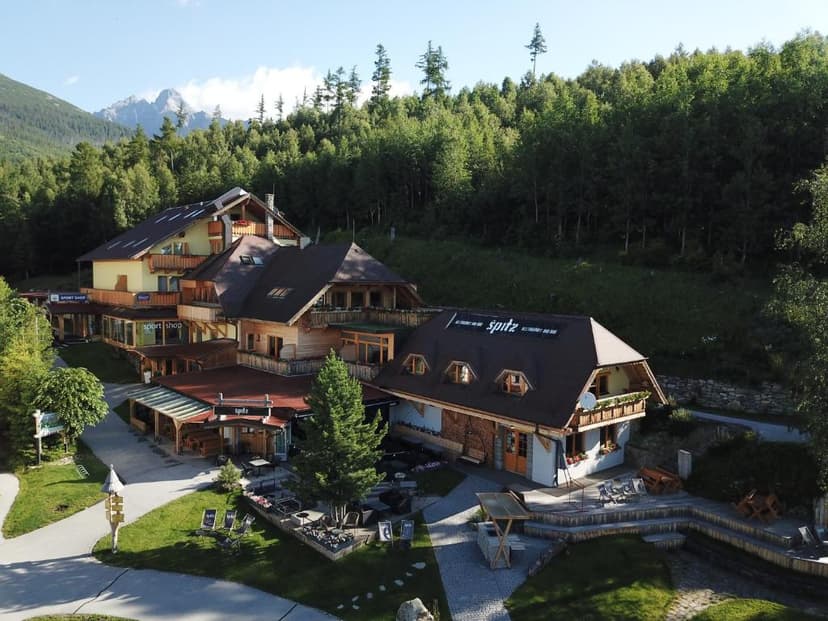 Alpine resort buildings with wooden balconies nestled against a dense green forest and distant mountains.