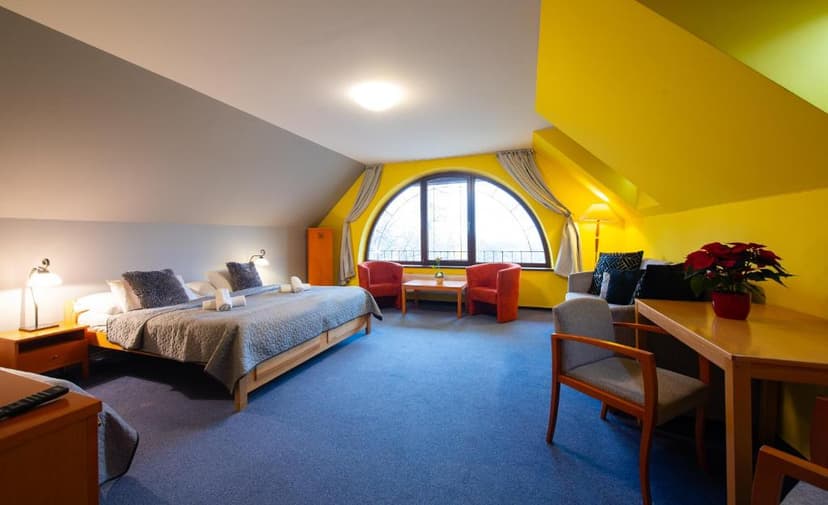 Attic hotel room with blue carpet, large bed, seating area, and arched window in Vila Park Lomnica Dve.