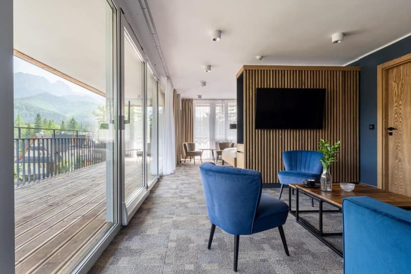 Hotel room interior with blue chairs, wood accents, and mountain view balcony in Zakopane.