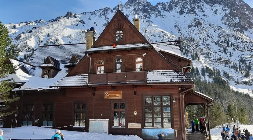 Wooden mountain hut with snow-covered roof against snowy peaks, Morskie Oko, Poland