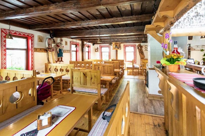 Rustic restaurant interior with wooden tables, benches, and exposed beam ceiling, possibly Koliba Tri.
