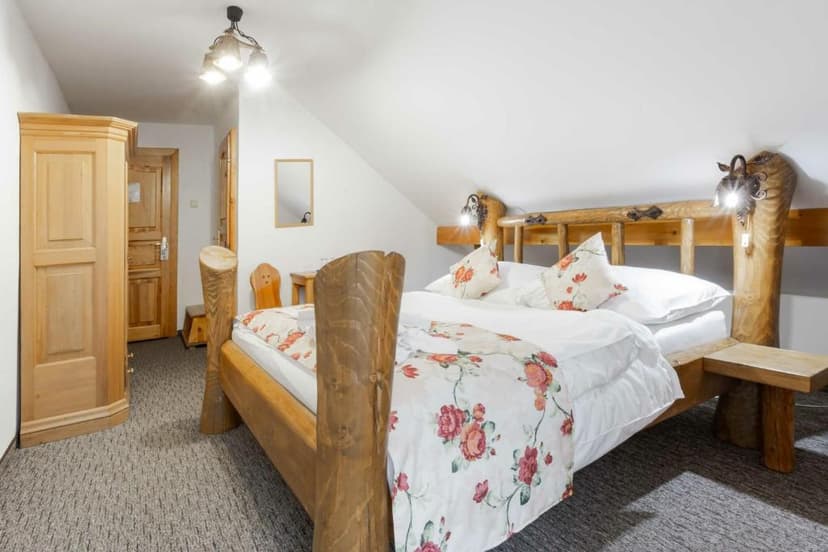 Bedroom with rustic wooden bed, floral linens, and sloped white ceiling, likely in a pension.