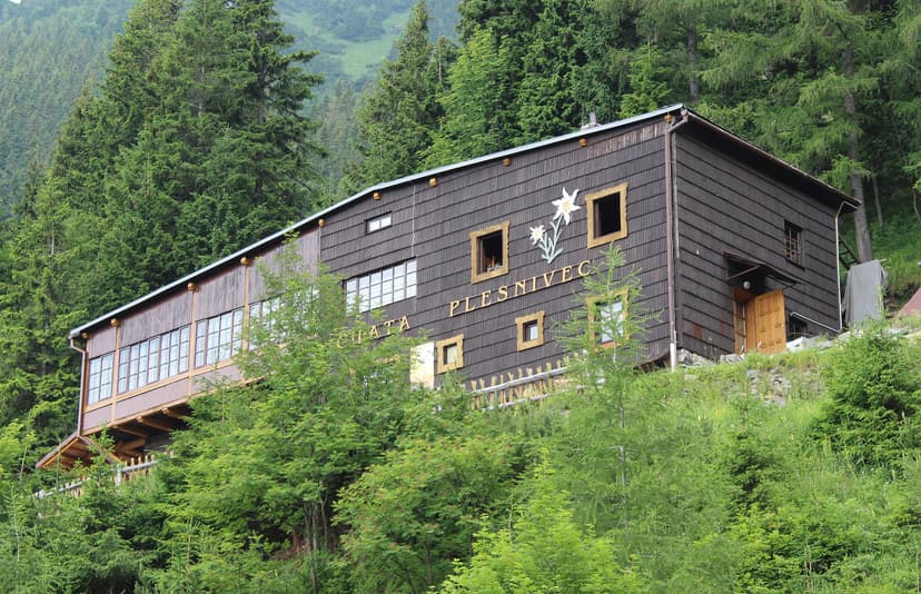 Chata Plesnivec wooden mountain hut surrounded by dense green forest on a hillside.
