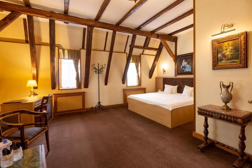 Hotel room with exposed dark wood beams, a large bed, and a desk area.