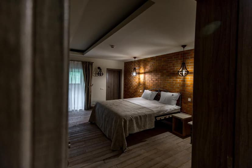 Bedroom with wooden floor, brick accent wall, and hanging pendant lights, viewed through a doorway.