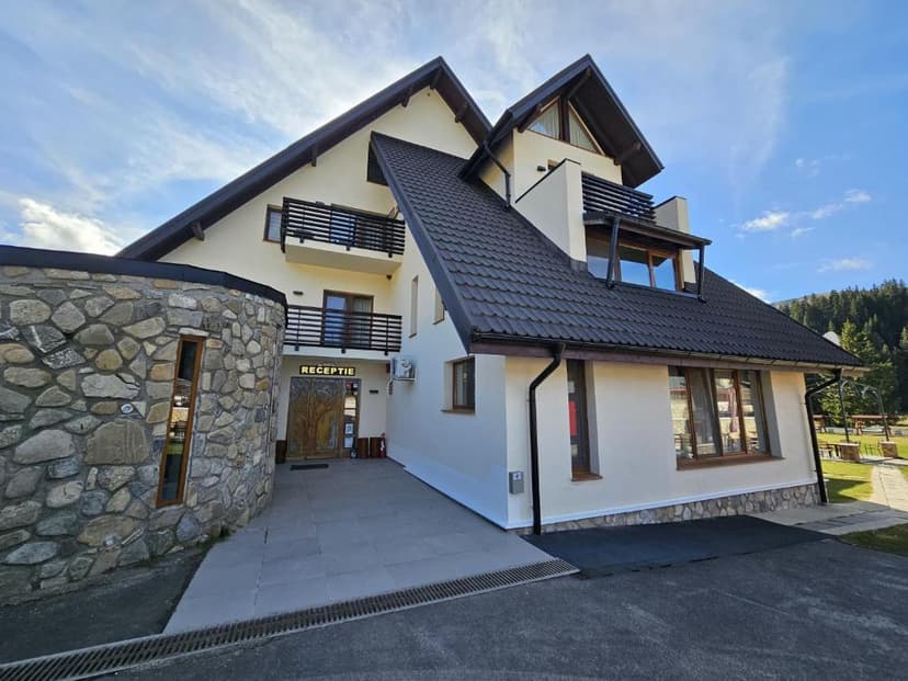 Two-story building with stone facade section and "RECEPTIE" sign under bright sky.