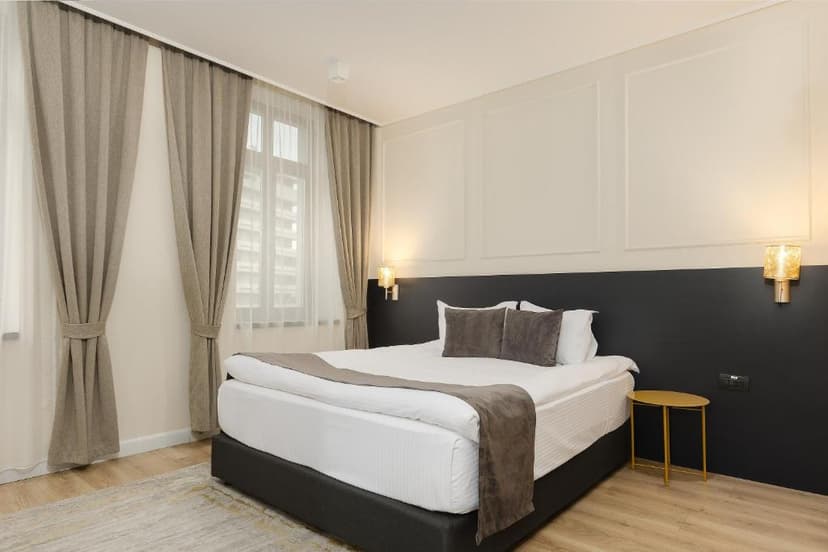 Hotel Atria room with a large bed, white linens, gray accents, and window with beige curtains.