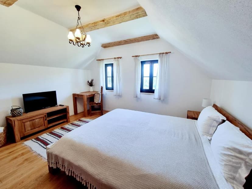 Attic bedroom with white walls, exposed wooden beams, and rustic wooden furniture.