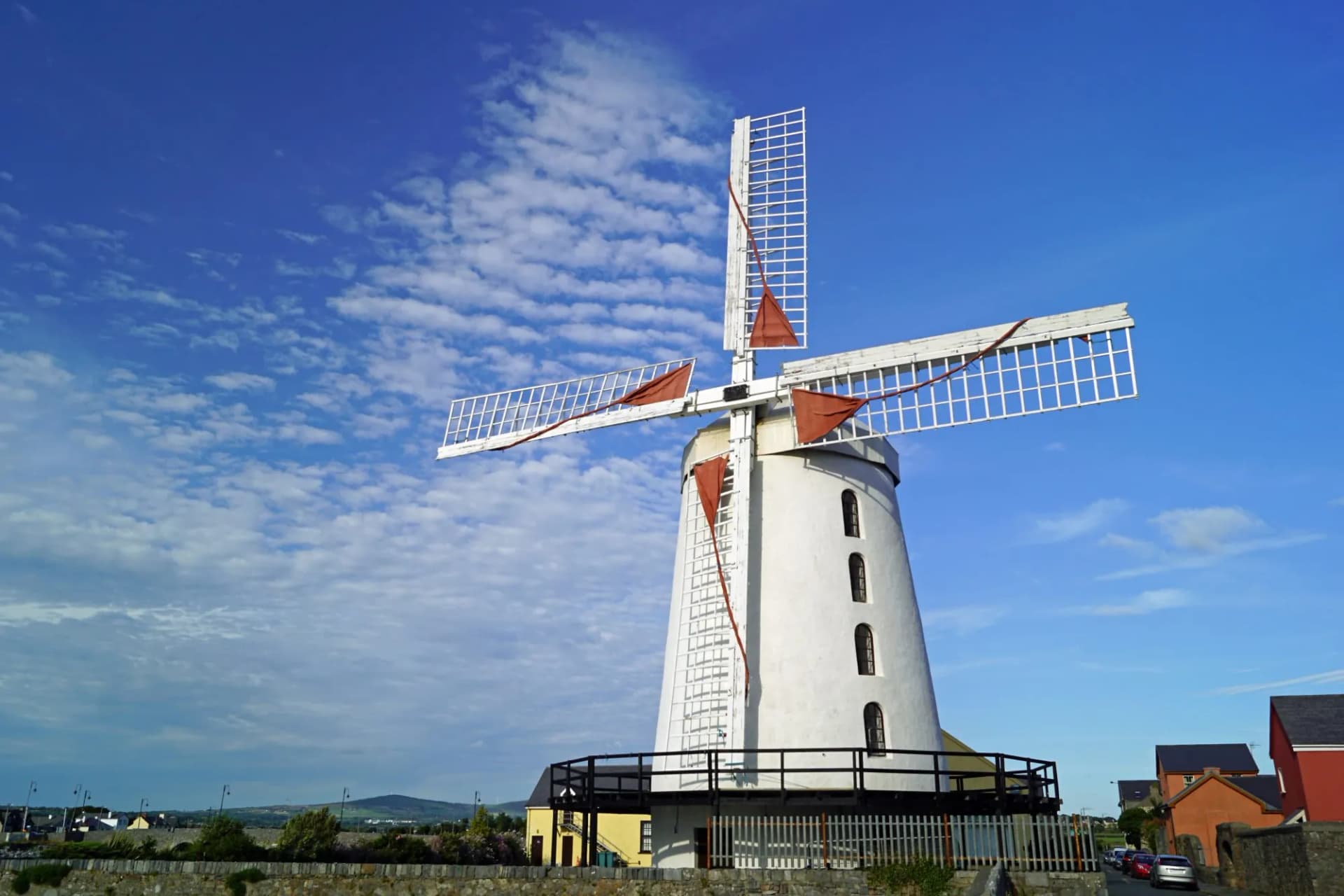 White Blennerville Windmill with red sails against a bright blue sky with scattered clouds.