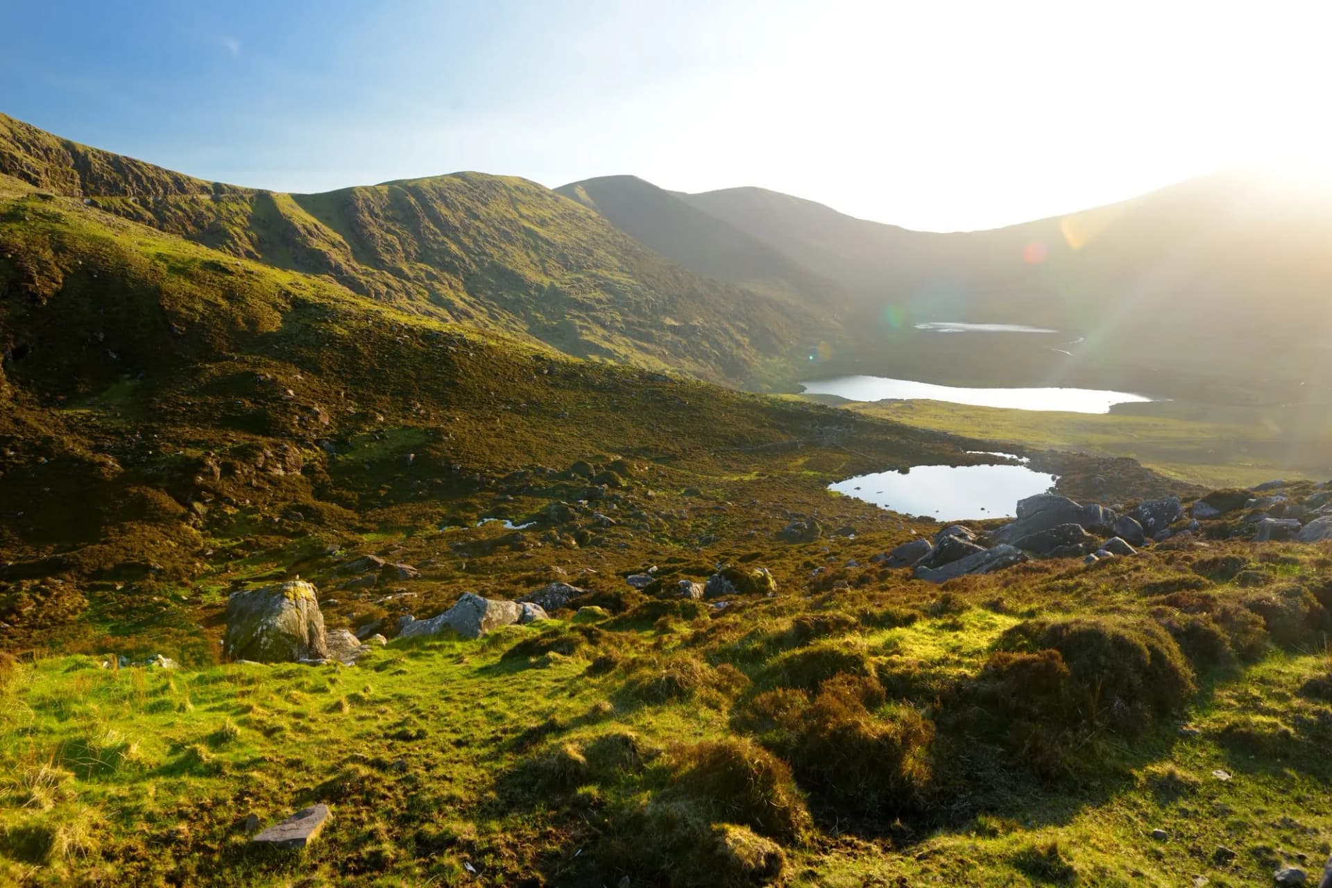 Green mountainsides overlooking lakes at Conor Pass, with bright sunlight flaring on the right.
