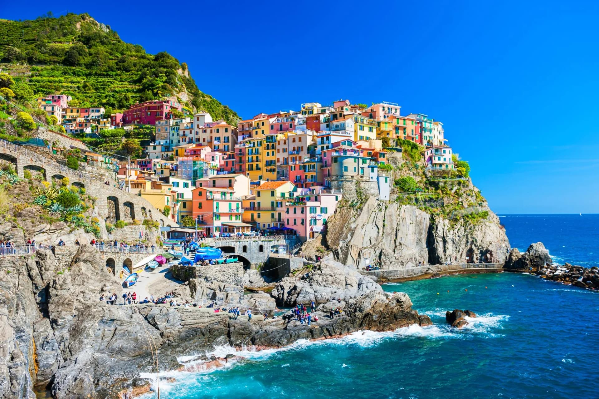 Colorful houses of Manarola in Cinque Terre clinging to steep cliffs above the bright blue Mediterranean Sea.