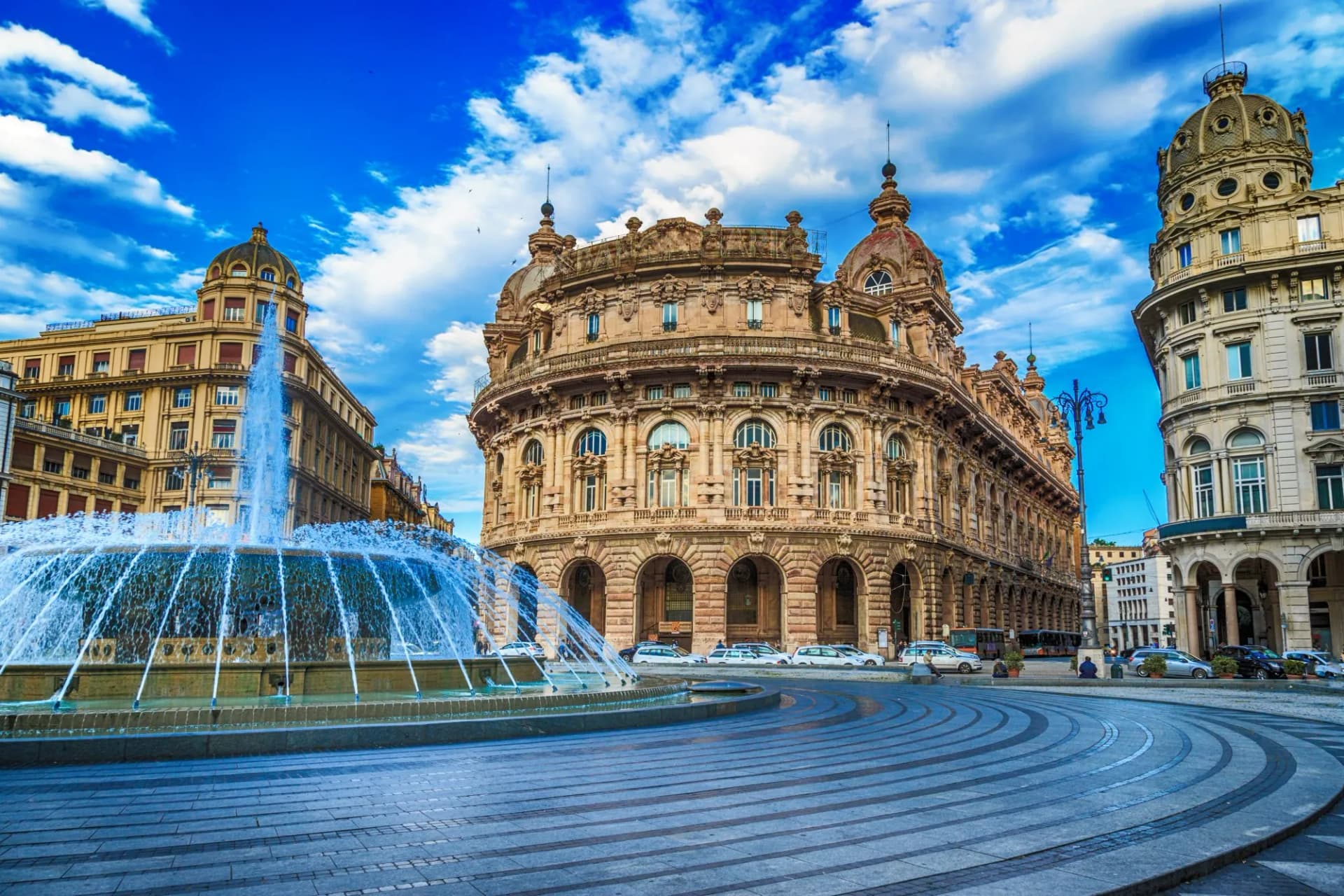Fountain spraying water in Piazza De Ferrari with ornate historic buildings under blue sky in Genoa.