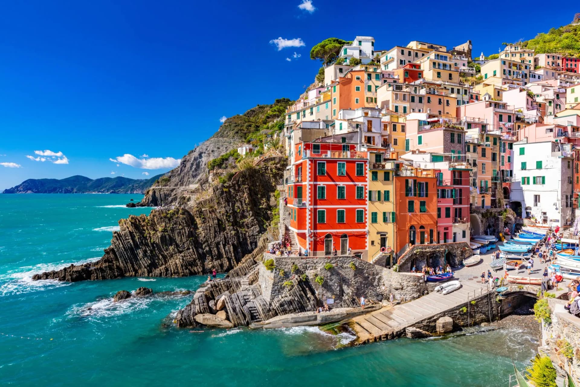 Colorful stacked houses on a cliff overlooking turquoise Mediterranean water in Riomaggiore.