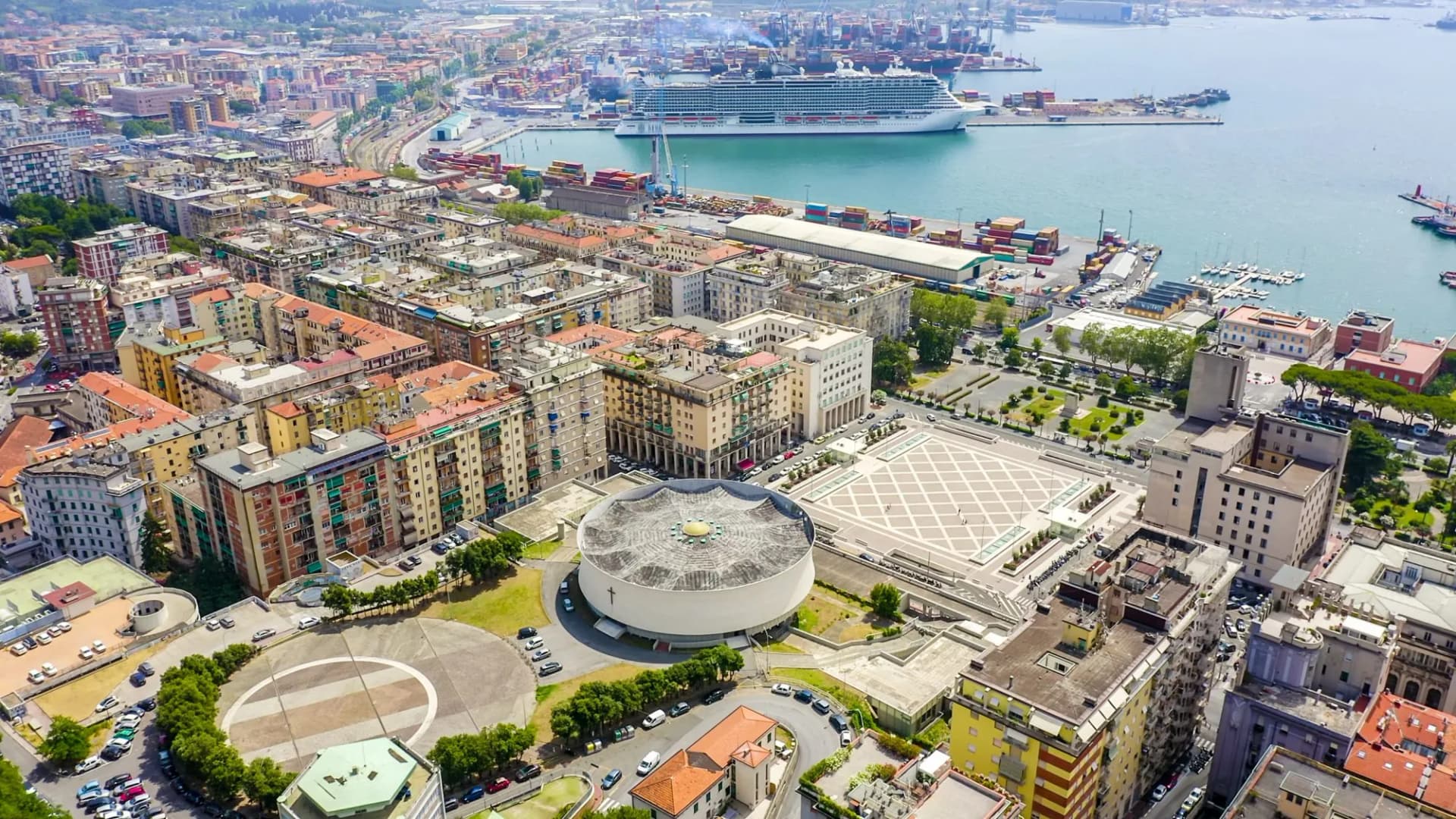 Aerial view of La Spezia city with dense buildings, a large square, and a cruise ship in the harbor.